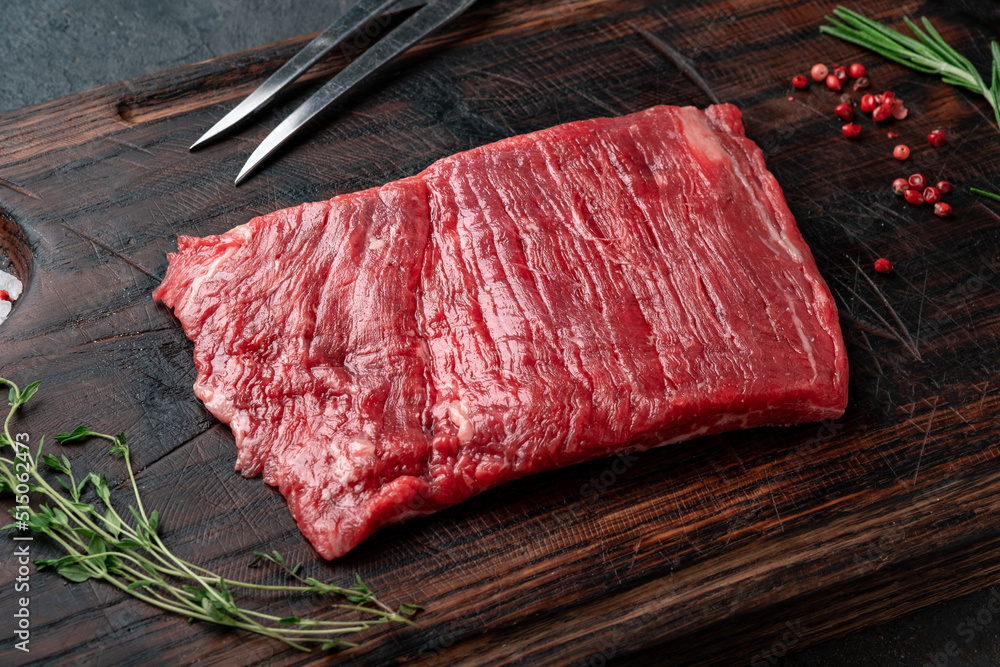 Raw flank steak on a wooden board with grilling seasonings, close up - obrazy, fototapety, plakaty 