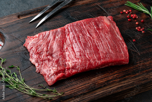 Raw flank steak on a wooden board with grilling seasonings, close up