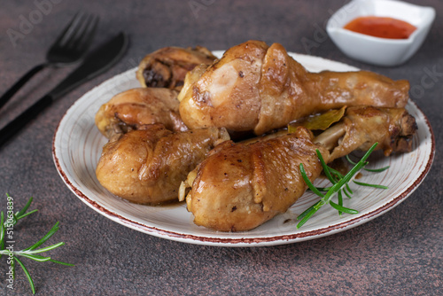 Baked chicken drumsticks in soy sauce with honey and rosemary on plate on brown background
