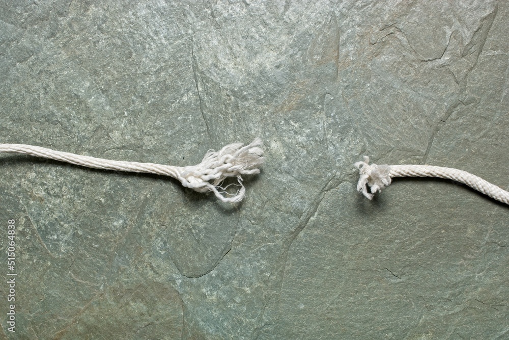 'Tension concept with frayed ends of snapped white braided rope hanging against rock face' Stock
