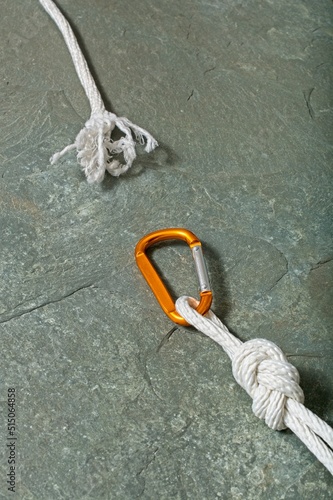 'Tension concept with frayed end of  white braided rope unlashed from offset-D type carabiner hanging against rock face' photo