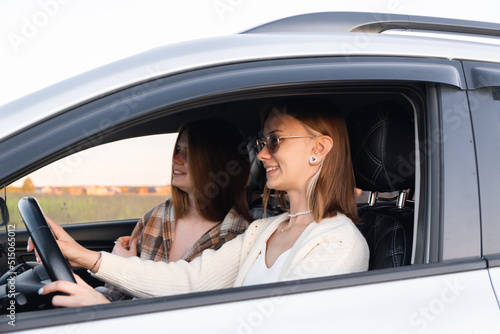Two young women laughing in the car during a summer road trip. Best friends have fun together as they drive through the countryside. A happy couple of girls relaxing on a road trip. © deine_liebe