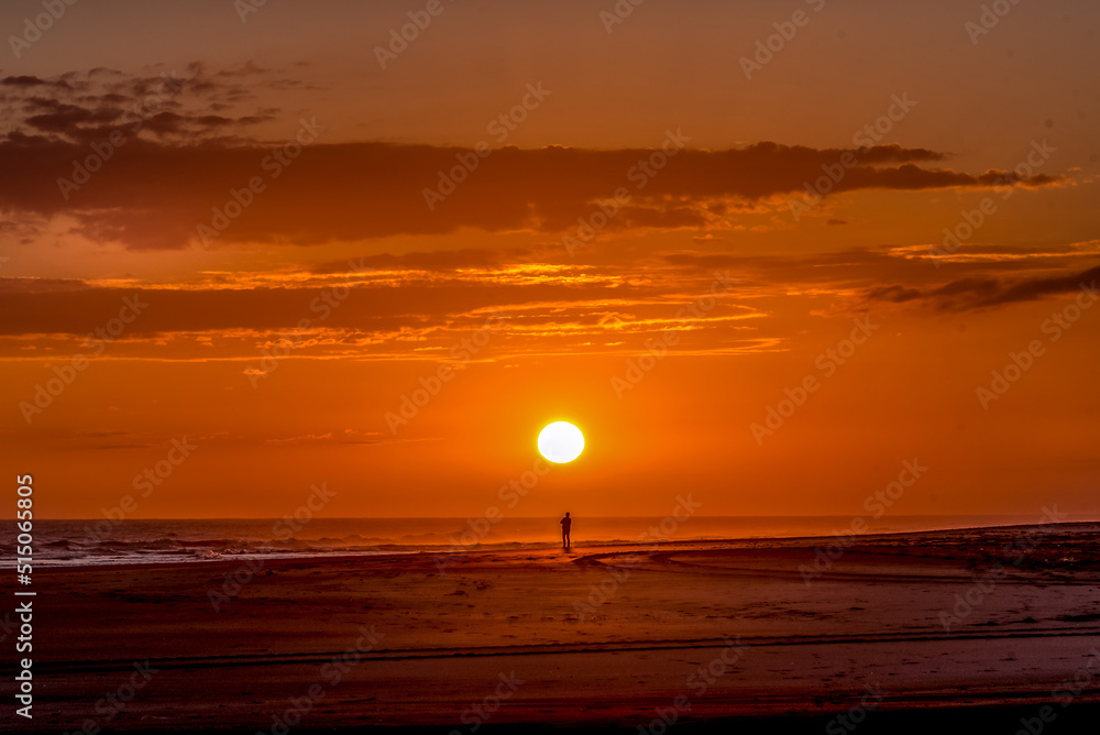 Silhouette of a man standing on the beach looking at a golden sunset ...