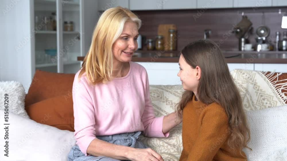 Happy middle aged mom talking to cute teen child daughter at home. 