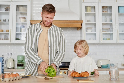 Waist up portrait of happy father and son cooking together at home in cozy kitchen interior