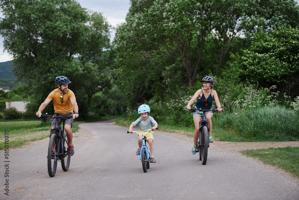 Young family with little child riding bicycles on road in village in summer. Young family with little child riding bicycles on road in village in summer.