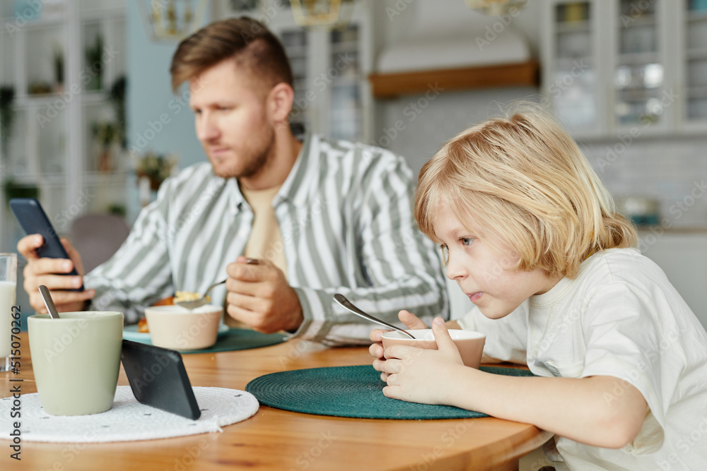 Side view portrait of father and son using smartphones at dining table and watching videos, copy space Side view portrait of father and son using smartphones at dining table and watching videos, copy space