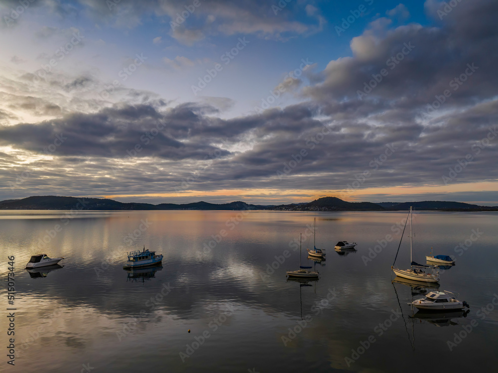 Aerial sunrise waterscape with boats, reflections and cloud filled sky