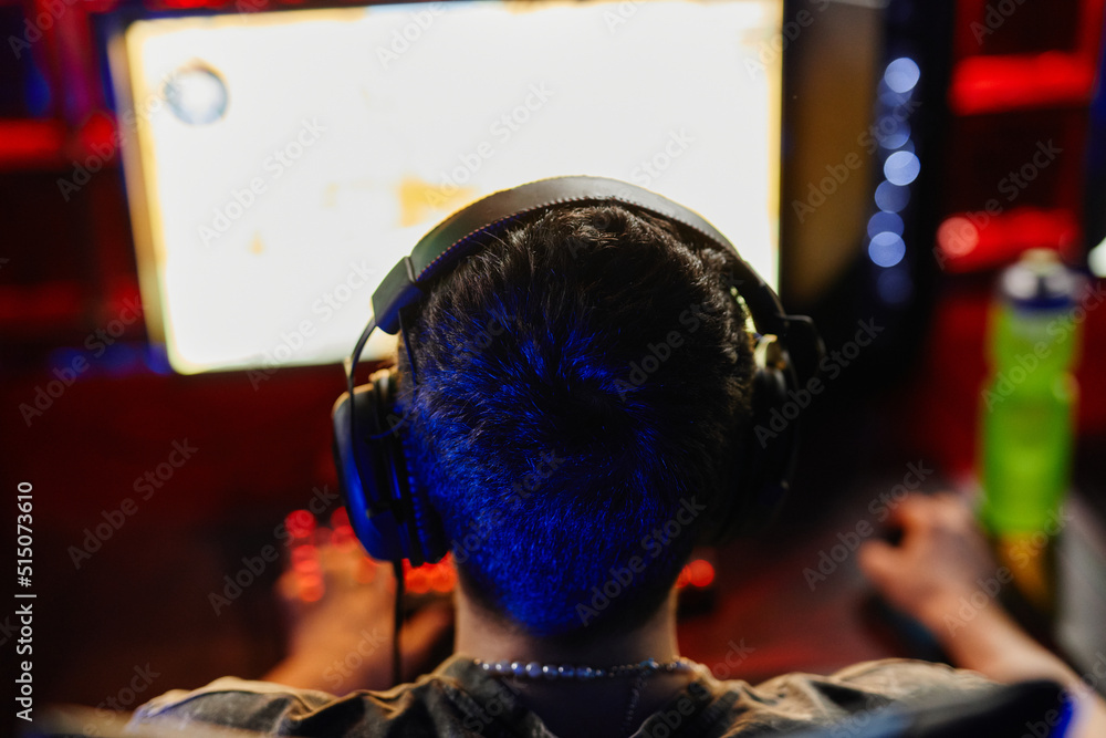 Obraz premium Back view at man playing video games in dark, focus on head with headphones, copy space