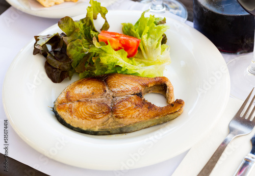 Delicious grilled bonito steak served with fresh tomatoes and lettuce on white dish..