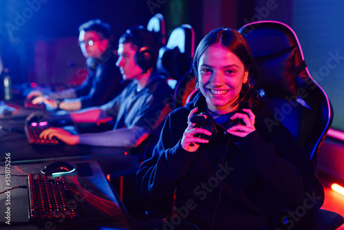 Portrait of young woman on cyber sports team smiling at camera cheerfully lit by neon light, copy space photo