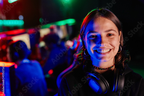 Close up portrait of young woman on e-sports team smiling at camera cheerfully lit by neon light, copy space