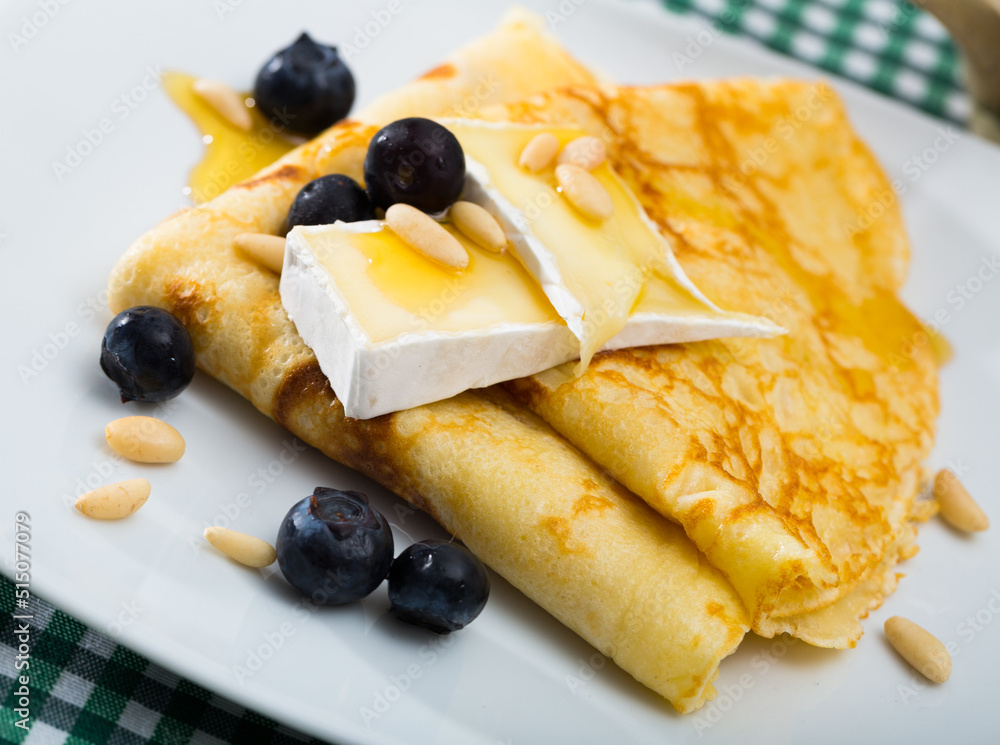 Delicate thin pancakes with brie slices, honey, toasted pine nuts garnished with fresh blueberry