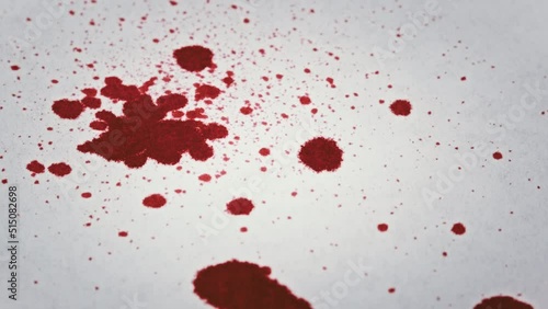 Drops of blood fall on white paper in macro. Red blood is absorbed into the white paper. Dripping Red Ink on Paper. Gore splatters on a white surface. Bloodstains reveal on white background. Close-Up.