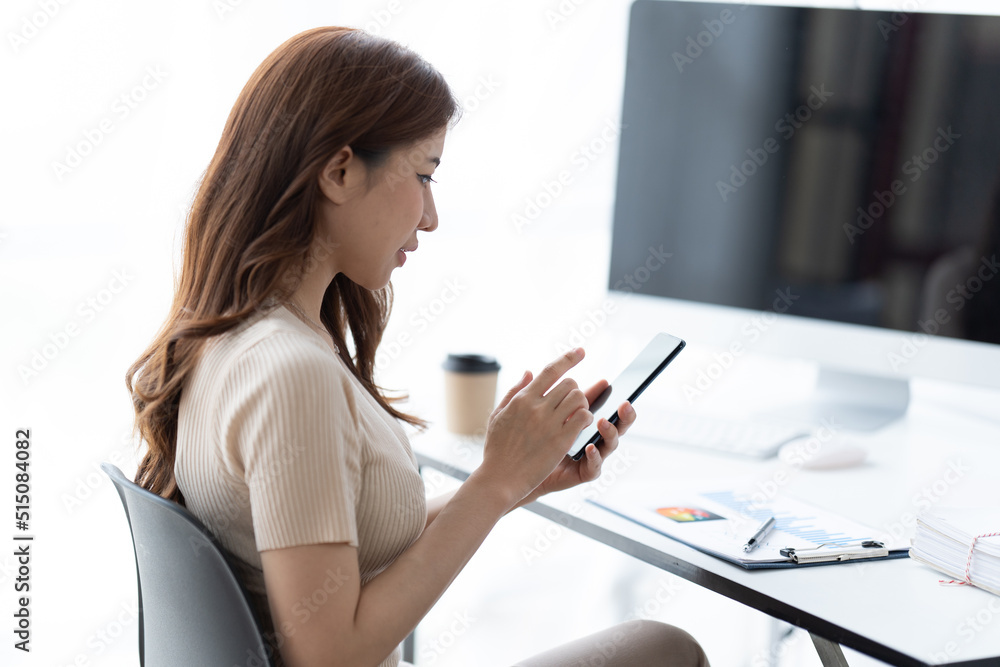 Portrait of smiling young woman with smartphone in her hands, sitting at table in front of laptop. Girl works on computer while sitting in office, checks email. Online marketing, distance education. Portrait of smiling young woman with smartphone in her hands, sitting at table in front of laptop. Girl works on computer while sitting in office, checks email. Online marketing, distance education.