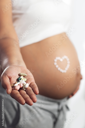 Pregnant woman latina with pills on right hand, white background, horizontal angle