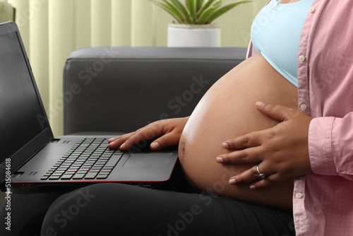 pregnant woman typing on laptop sitting on couch in living room
