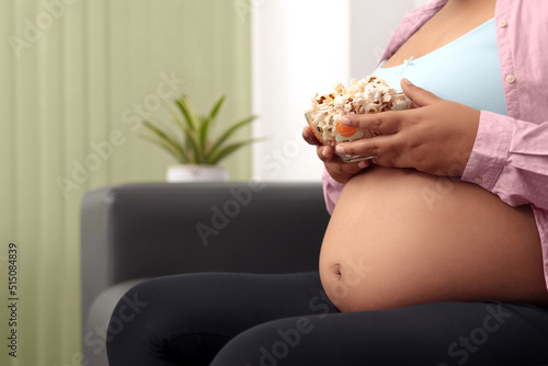 Pregnant woman siting on couch in living room, eating corn pop
