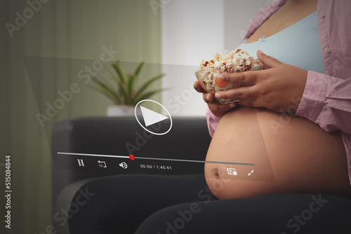 Concept business streaming service, pregnant woman watching video streaming on internet, eating corn pop