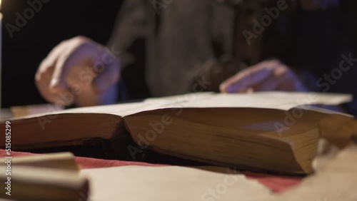 Old ancient book.Historical period reenactment.
Historical era man reading a book by candlelight.
