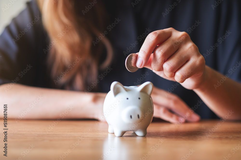 Closeup image of a woman putting coin into piggy bank for saving money concept - obrazy, fototapety, plakaty 