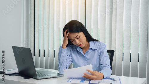 Asian woman manager is stressed and has a headache about faulty work documents at her office.