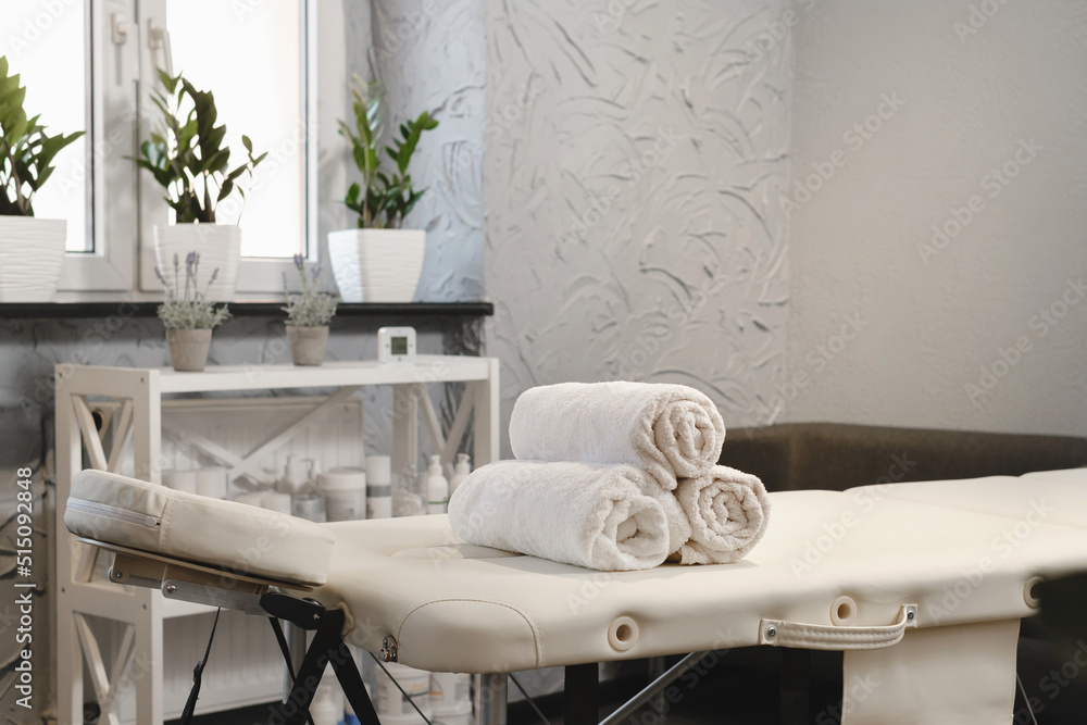 Rolled white towels on massage table in empty salon. Interior of aesthetic  clinic, nobody. Modern cabinet of physiotherapist. Empty room with plants  of beautician in wellness center. Copy space Photos | Adobe