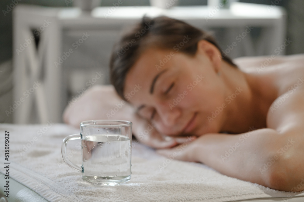 Beautiful young woman with cup of water relaxing in spa salon. Woman in spa in sauna resting. Hot steam relaxation. skin detox therapy. Enjoy the warm air. The girl drinks mineral water. Beautiful young woman with cup of water relaxing in spa salon. Woman in spa in sauna resting. Hot steam relaxation. skin detox therapy. Enjoy the warm air. The girl drinks mineral water.