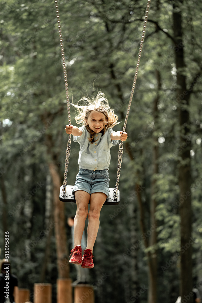 a girl walks in the park, swings on a swing
