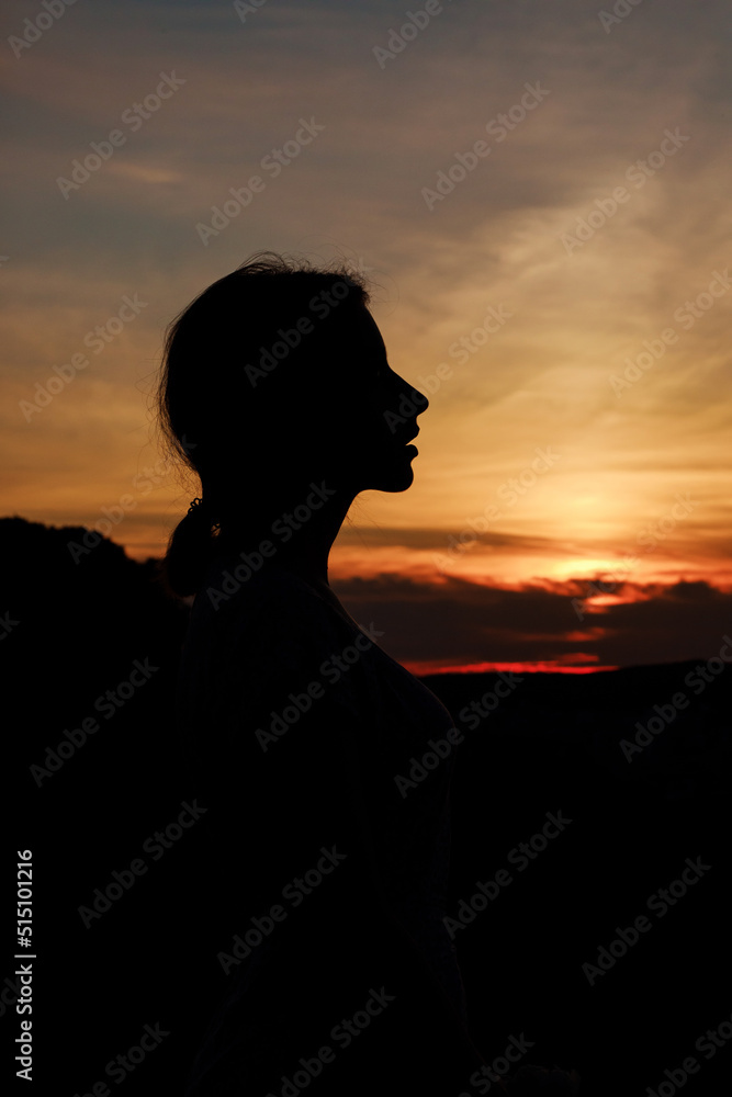 Close up silhouette of a woman at sunset. Image against the sun and orange sky.