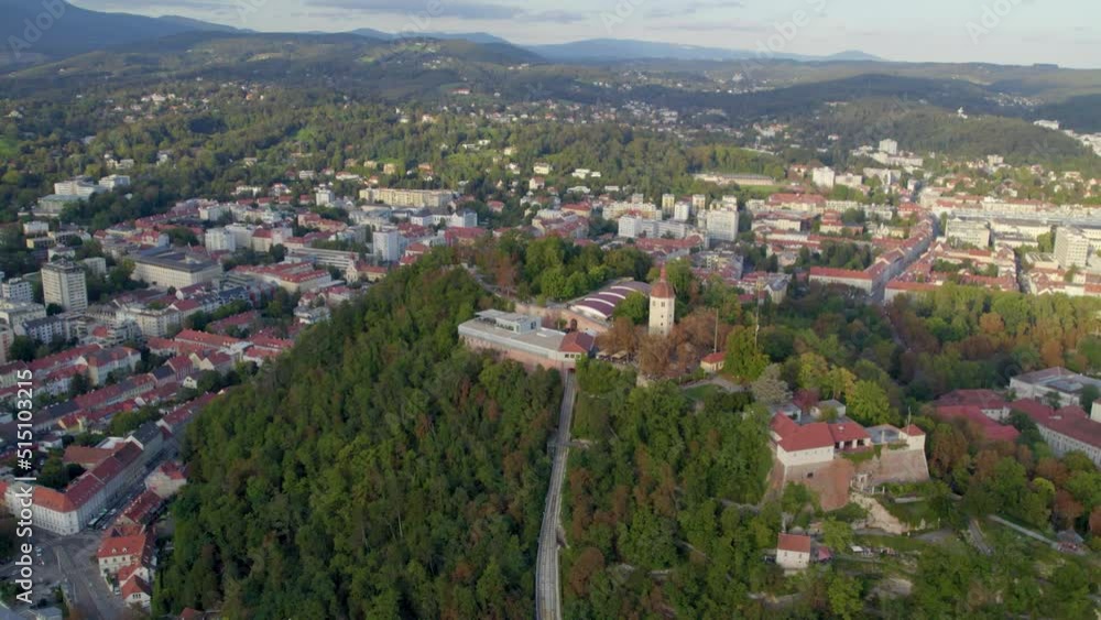 Aerial view flying high around historic Glockenturm tower overlooking Graz Schloßberg dense hilltop woodland cityscape Aerial view flying high around historic Glockenturm tower overlooking Graz Schloßberg dense hilltop woodland cityscape