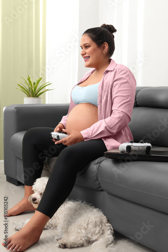 Pregnant woman playing playstation sitting on couch, laptop, living room