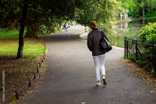 Canvas Print Slim woman in white jeans and black jacket walking in a park