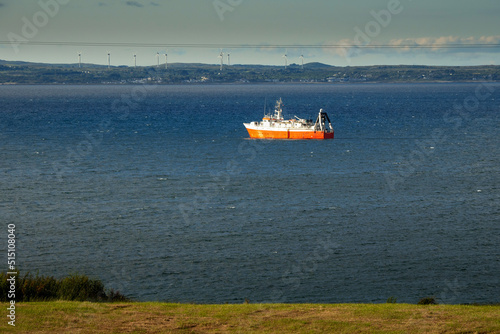 Small fishing ship with red hull in the ocean. Galway bay, Ireland. Food industry and supply concept. Cloudy sky and dark color water surface. photo