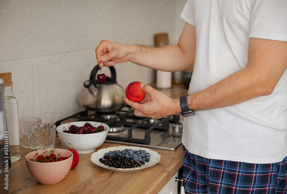 The guy chooses between cherries and nectarine. The guy eats fruit and berries for breakfast. Healthy lifestyle. Summer ration. Cherry, blueberry, currant and nectarine