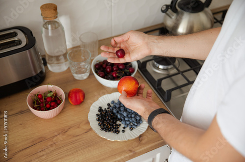 Obraz na płótnie The guy chooses between cherries and nectarine. The guy eats fruit and berries for breakfast. Healthy lifestyle. Summer ration. Cherry, blueberry, currant and nectarine w salonie