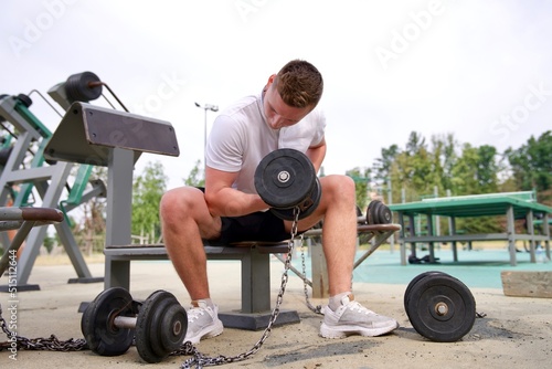 portrait of handsome happy strong athletic man athlete bodybuilder training with dumbbells outdoors at open air gym at summer  gain hands and shoulders muscles. Bodybuilding fitness  healthy lifestyle