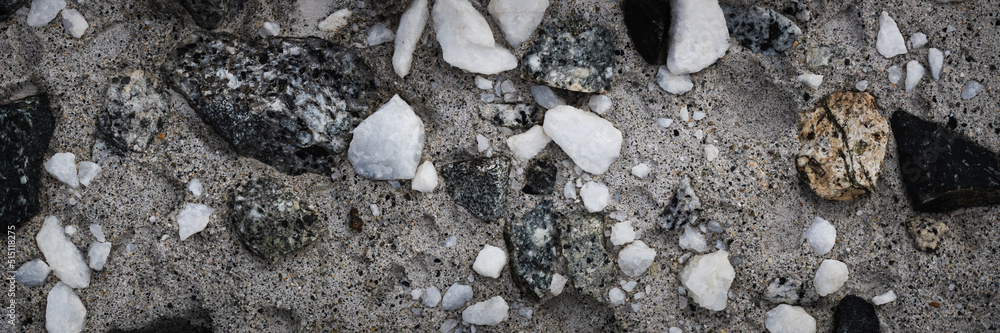 Concrete wall texture with pebbles. Decorative rough concrete surface with white, black and gray stones. Wide panoramic texture for background and design.
