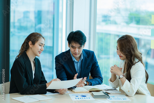 A young multi-ethnic business team in a high-key office sits on a laptop and does paperwork with happy smiles. Group of Asian businessmen team meeting in modern office Design and Concept Planning