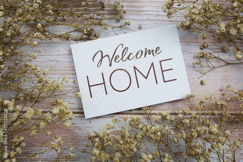 Welcome Home text on paper card with flower decoration on wooden background photo