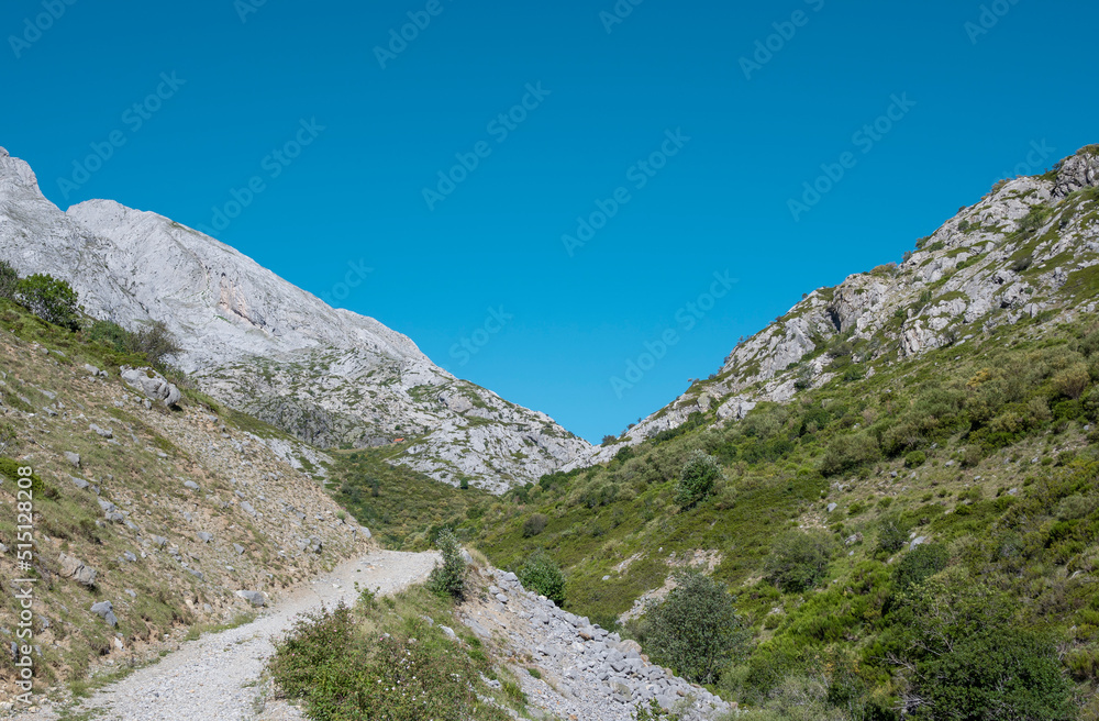 Camino de tierra entre montañas rocosas en el valle de Mazobre del parque natural de la montaña Palentina, España Camino de tierra entre montañas rocosas en el valle de Mazobre del parque natural de la montaña Palentina, España