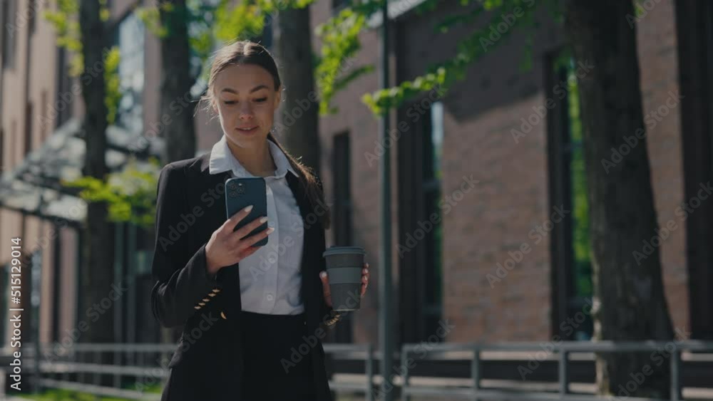 Successful smiling woman holding cardboard cup of takeaway coffee and using smartphone outdoors. Dark haired caucasian woman checking social networks while walking on city street. Successful smiling woman holding cardboard cup of takeaway coffee and using smartphone outdoors. Dark haired caucasian woman checking social networks while walking on city street.
