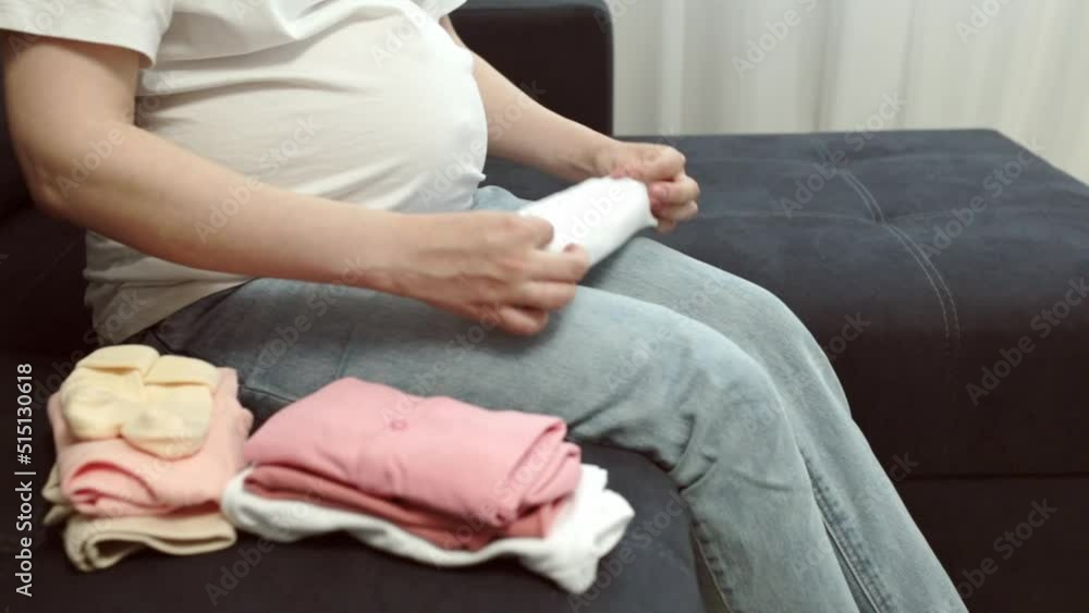 Pregnant woman sits on the bed and prepares things for the birth of a child Pregnant woman sits on the bed and prepares things for the birth of a child