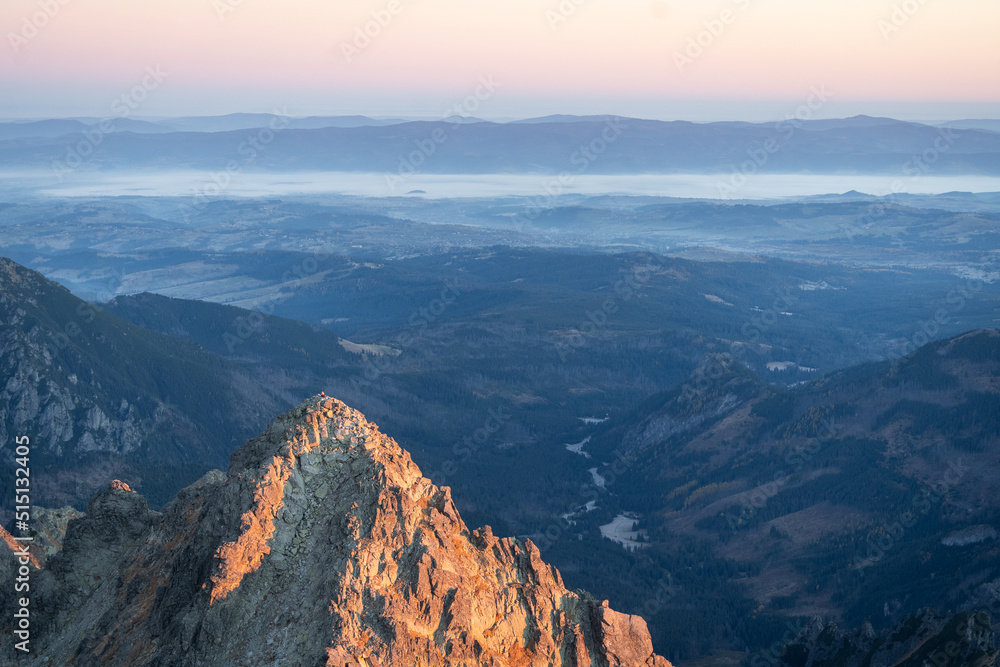 Prominent peak catching sunrise light with mountain range and foggy valley in the background