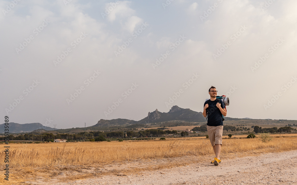 Montañero caucásico, caminando por un camino con su mochila, con expresión relajada y feliz. Fotografía horizontal, con espacio para texto. Montañero caucásico, caminando por un camino con su mochila, con expresión relajada y feliz. Fotografía horizontal, con espacio para texto.