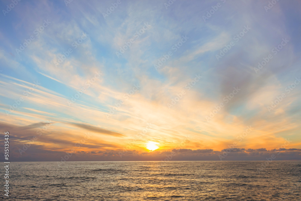 Sunset over the water surface of the sea horizon and cirrus clouds.