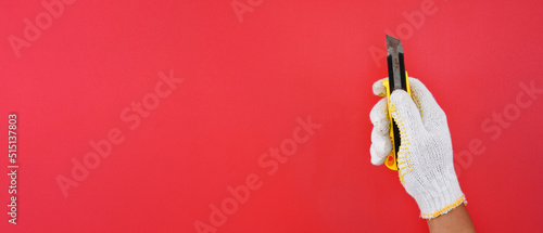 Hand wearing white gloves holding yellow cutter knife isolated red background
