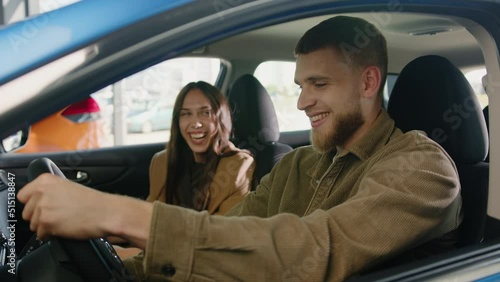 A young happy couple looks at each other in a good mood sitting in the cabin of a new car. Buying at a car dealership