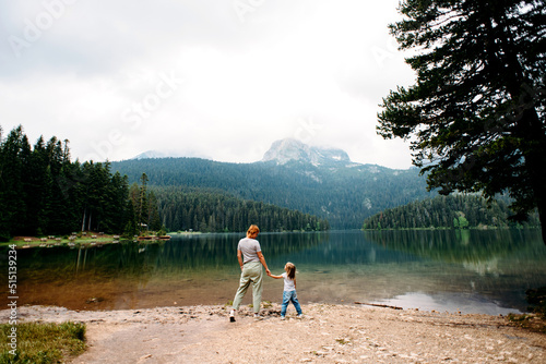 Mom and toddler daughter stand and look at Black Lake, Durmitor, Montenegro. Travel with kids. Family vacation. People and nature