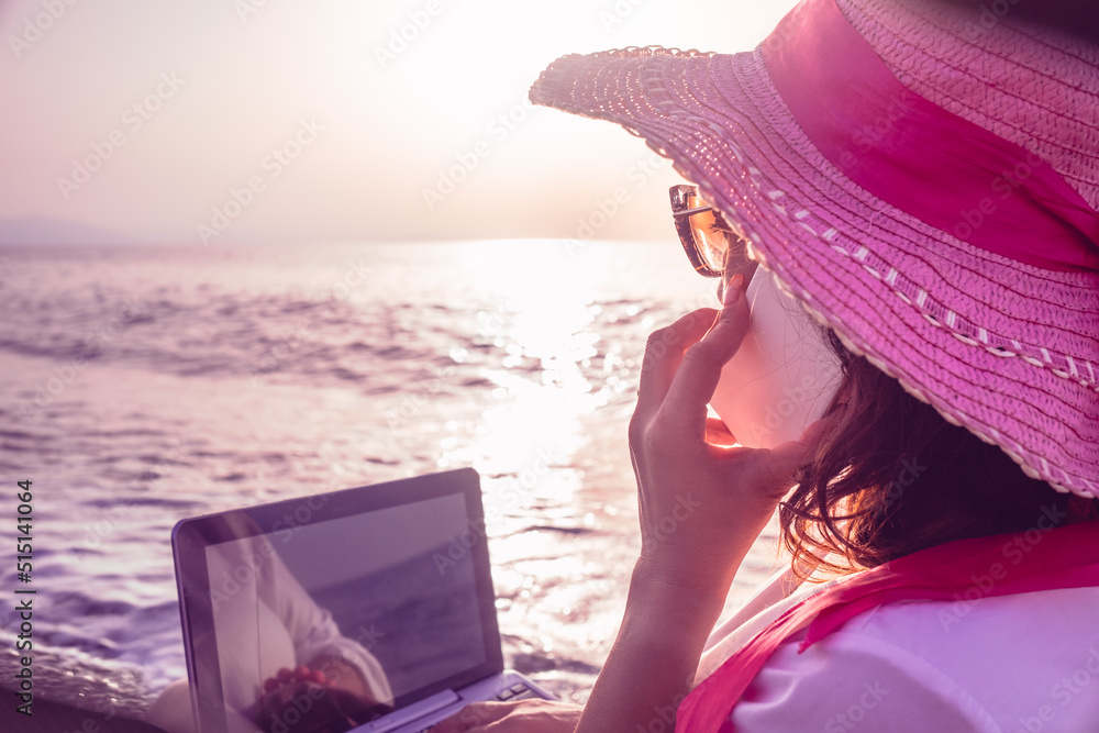 woman smart working on the beach with phone and laptop seen from behind